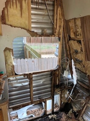Wooden trailer frame that is partly rotted with aluminum wall attached behind