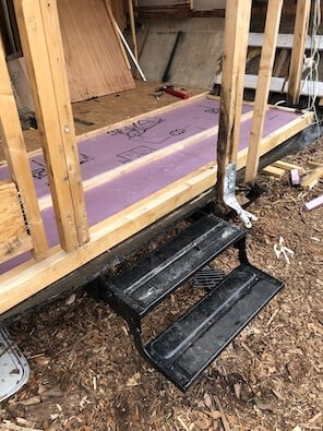 black metal stairs descending from wooden frame, purple styrofoam insulation in between floor joists